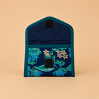 A small fabric pouch or organizer with a navy blue tropical leaf print on the lower half and a solid dark teal upper half, shown against a solid beige background.