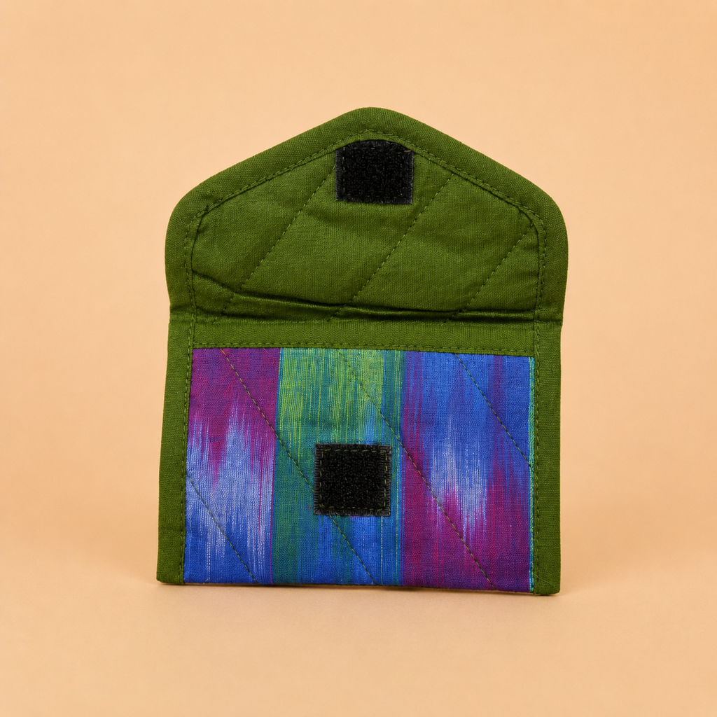 A small quilted fabric pouch or card holder in olive green with a colorful striped panel in blue, green, and purple, featuring two black hook-and-loop closures, shown on a solid peach background.