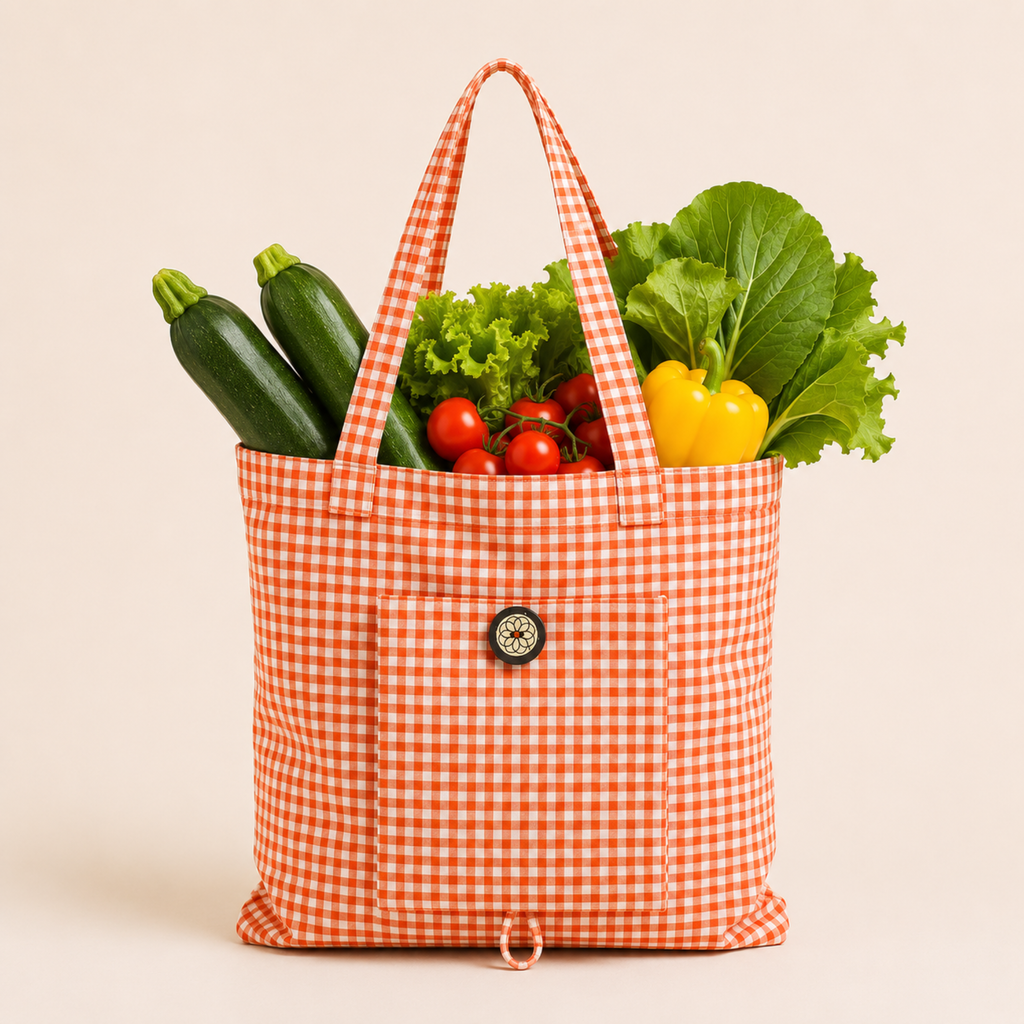 An orange and white gingham fabric tote bag filled with fresh vegetables, including cucumbers, tomatoes, lettuce, and a yellow bell pepper, set against a solid light beige background.