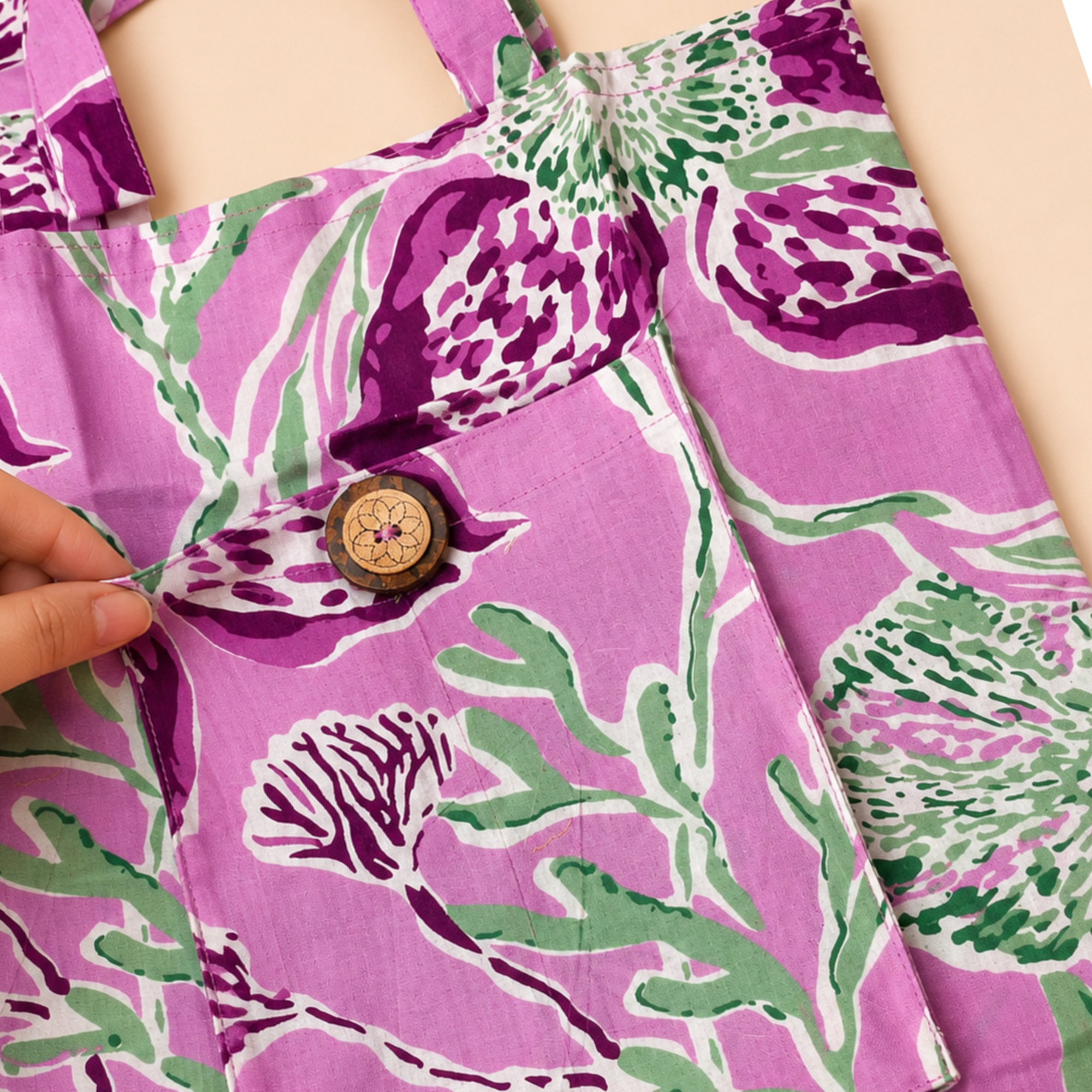 A close-up of a pink printed garment with a purple and green floral pattern, featuring a decorative wooden button and a hand adjusting the fabric.