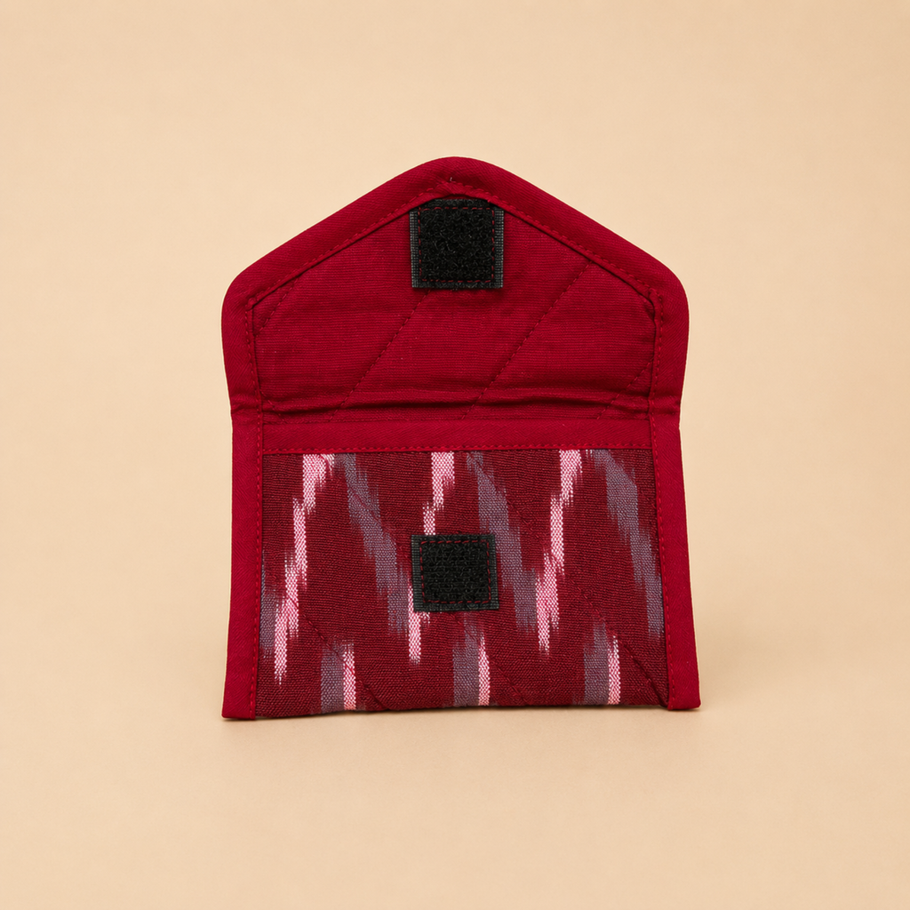 A small red fabric pouch with a quilted top section and a patterned lower pocket featuring pink, gray, and red ikat-style zigzags. The pouch has two black hook-and-loop closures and is photographed on a solid beige background.