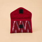 A small red fabric pouch with a quilted top section and a patterned lower pocket featuring pink, gray, and red ikat-style zigzags. The pouch has two black hook-and-loop closures and is photographed on a solid beige background.