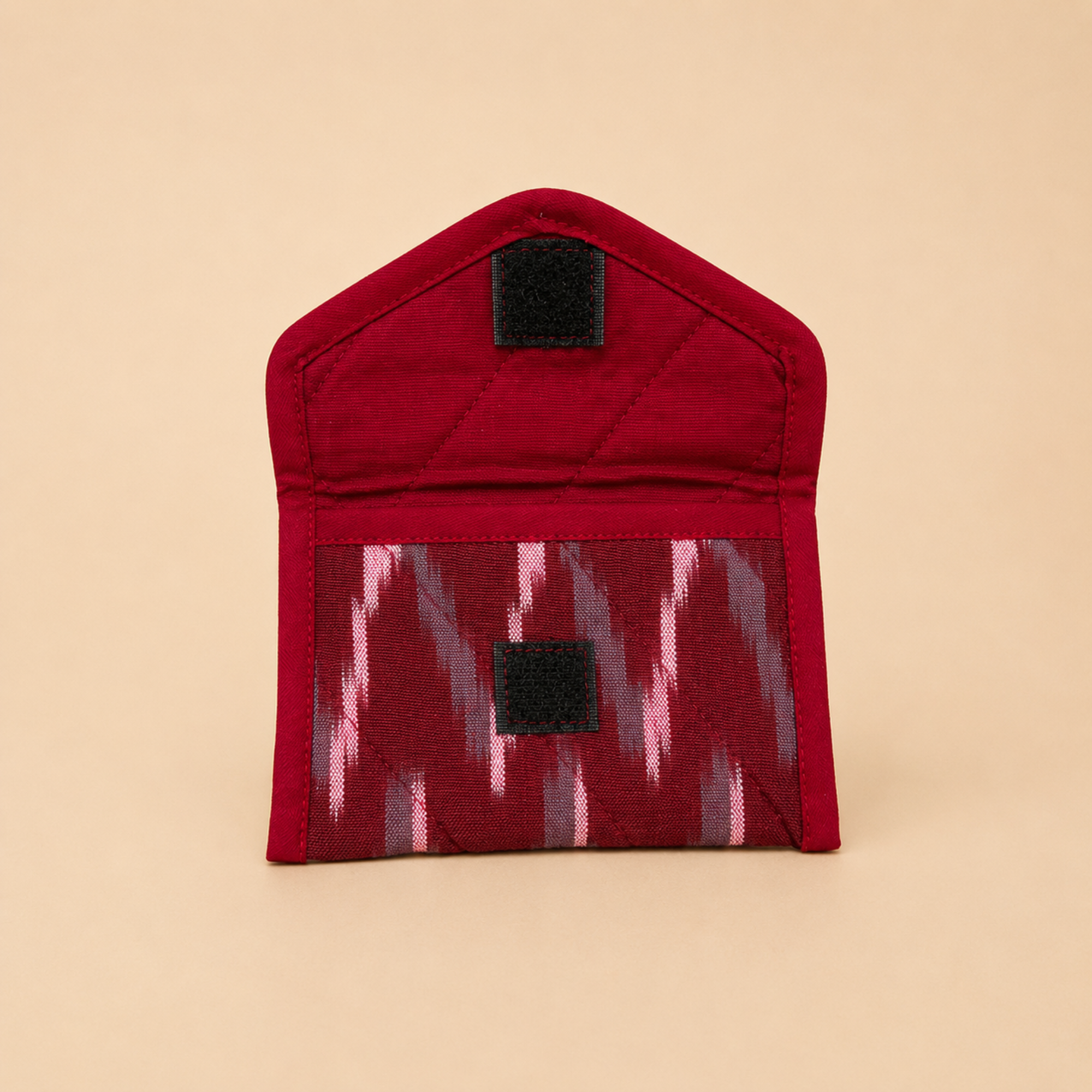 A small red fabric pouch with a quilted top section and a patterned lower pocket featuring pink, gray, and red ikat-style zigzags. The pouch has two black hook-and-loop closures and is photographed on a solid beige background.