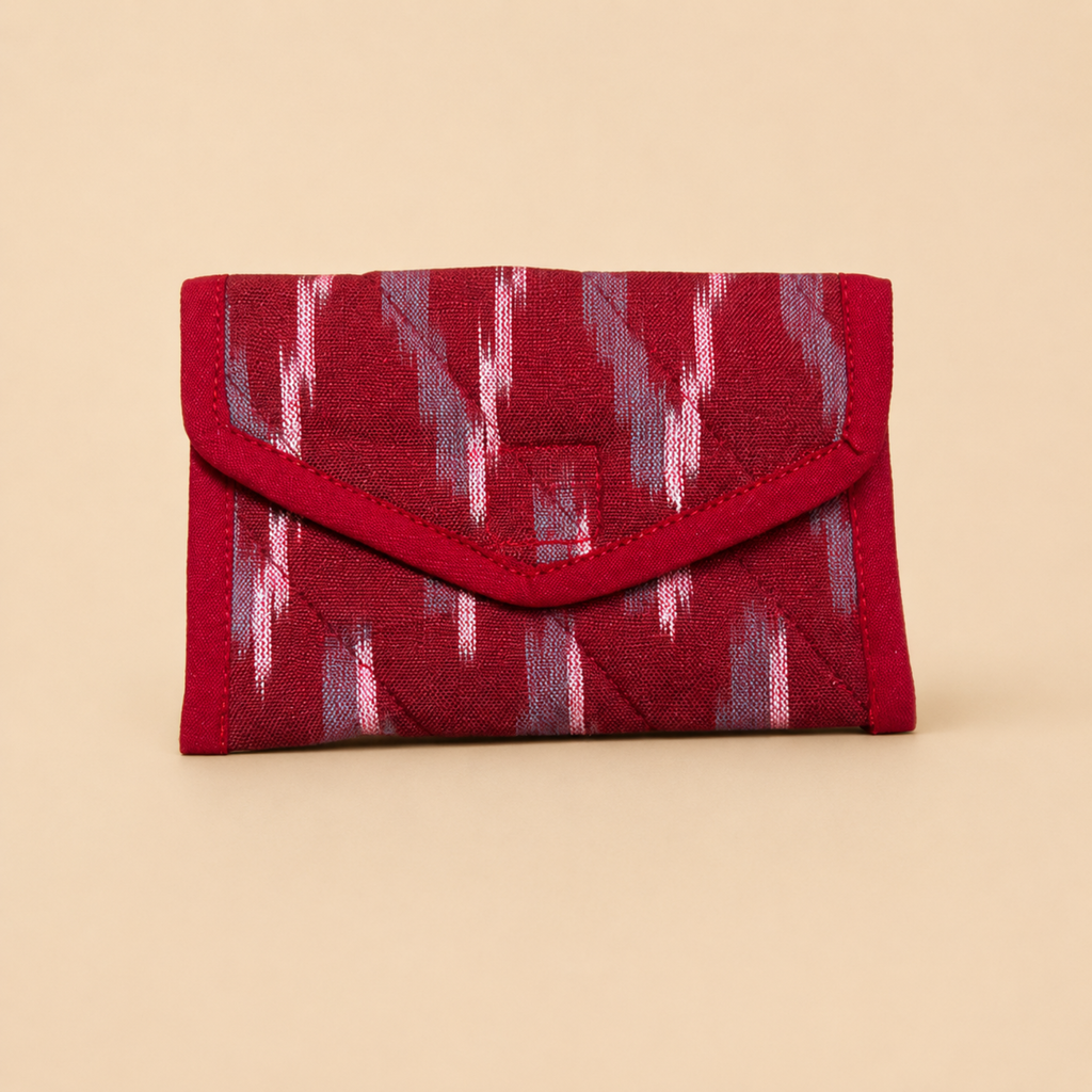 A small red envelope-style wallet with a quilted texture and an ikat pattern in red, pink, and gray, set against a solid beige background.