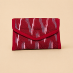 A small red envelope-style wallet with a quilted texture and an ikat pattern in red, pink, and gray, set against a solid beige background.